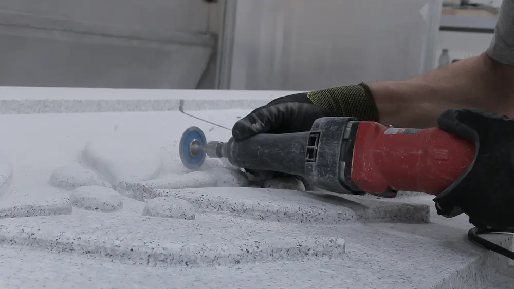 Profissional a trabalhar com ferramenta manual os detalhes em relevo de uma peça de pedra natural